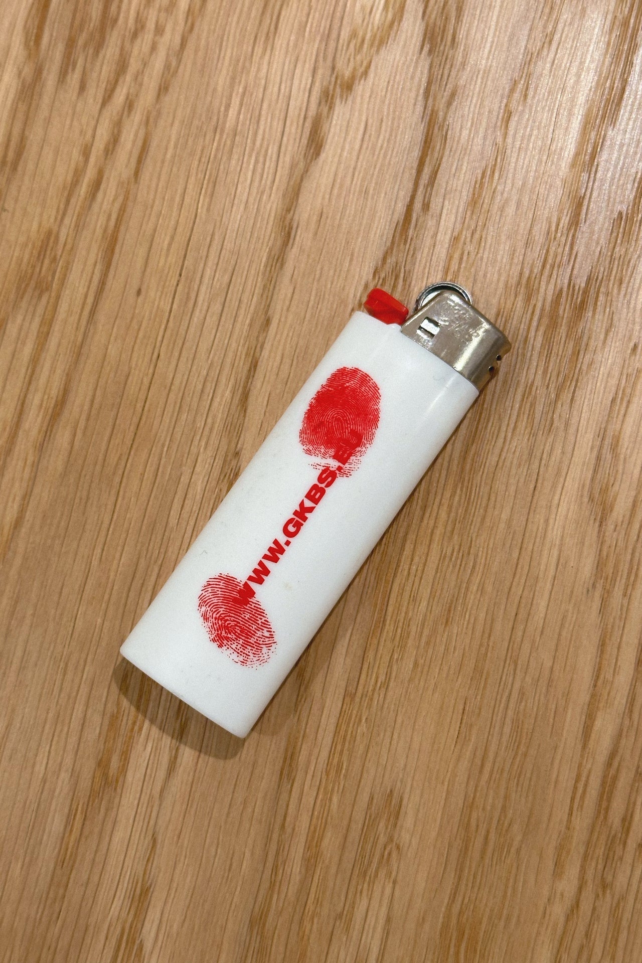 Rückseite des Wien Streetwear BIC Feuerzeugs, rote Fingerabdrücke und GKBS URL auf weißem Gehäuse