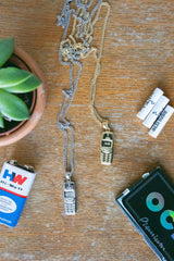Nokia 3310 Pendant Necklace Silber und Gold im Vergleich – beide Varianten mit Curb Chain auf Holz