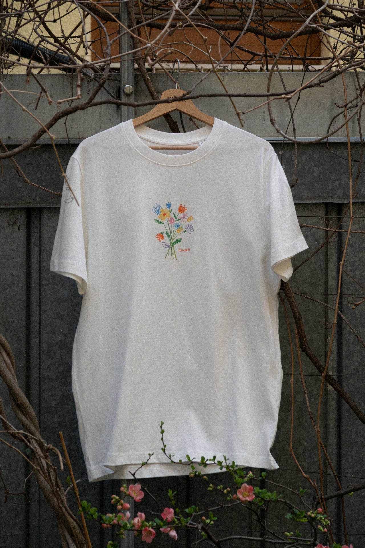 Off White Loose Fit T-Shirt Vorderseite, kleiner bunter Blumenstrauß-Print mit GKBS Schriftzug, Bio Baumwolle Wien