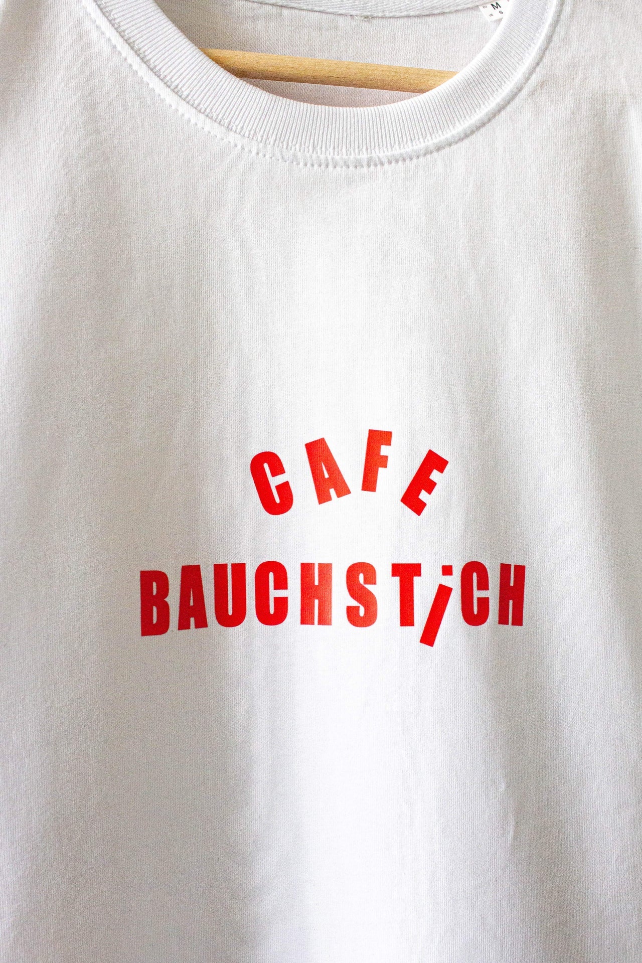 Nahaufnahme roter CAFE BAUCHSTICH Stickerei auf weißem Bio Baumwolle T-Shirt, Detailansicht