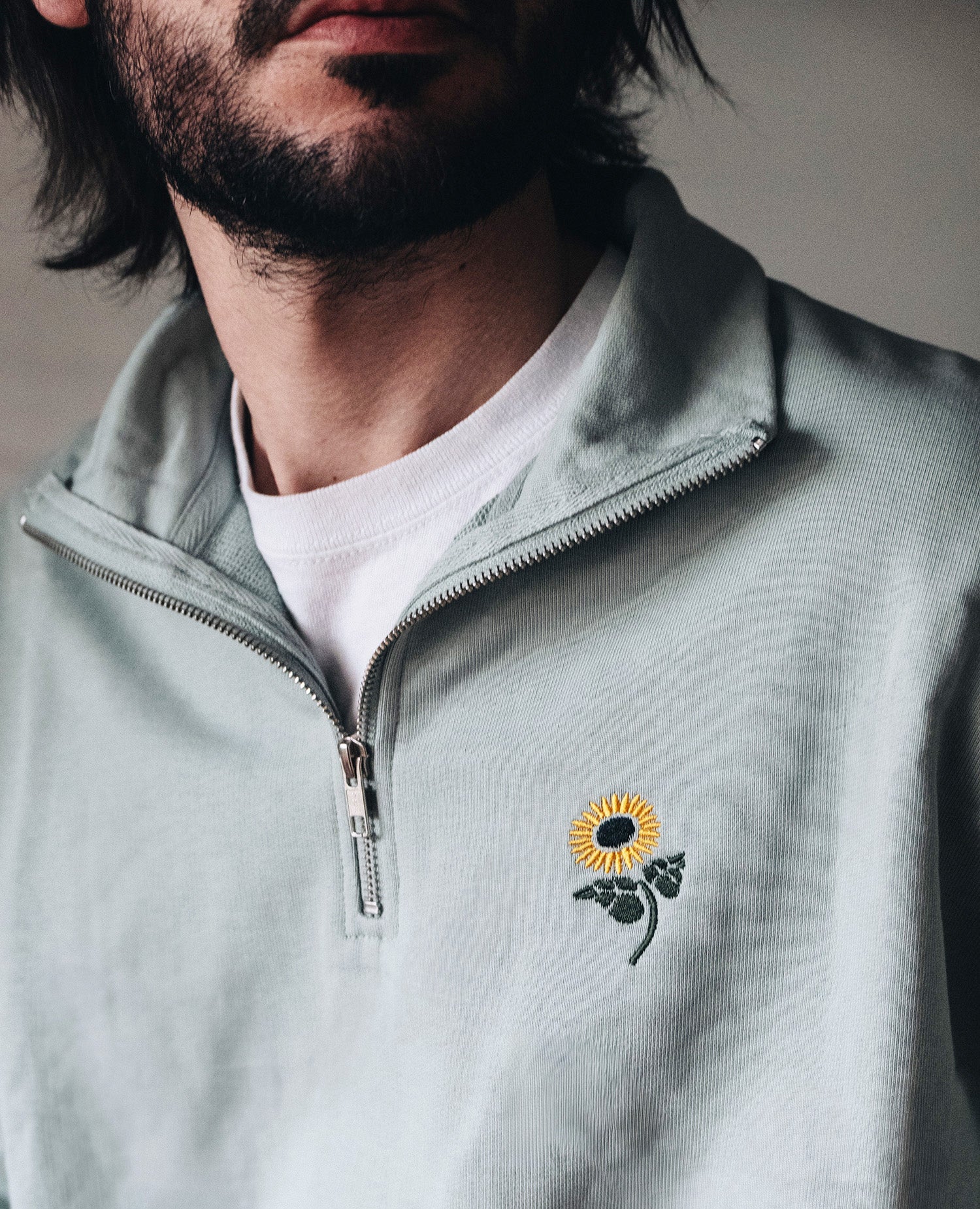 Half-Zip Sweatshirt Salbeigrün von NKSP – Stehkragen, Reißverschluss und Sonnenblumenstickerei am Model