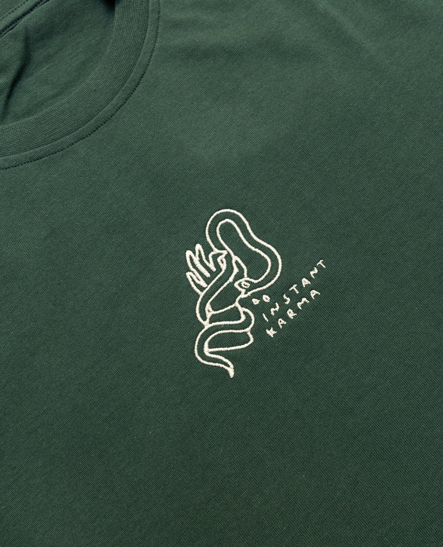 Instant Karma T-Shirt Dunkelgrün von NKSP – Nahaufnahme der cremefarbenen Stickerei